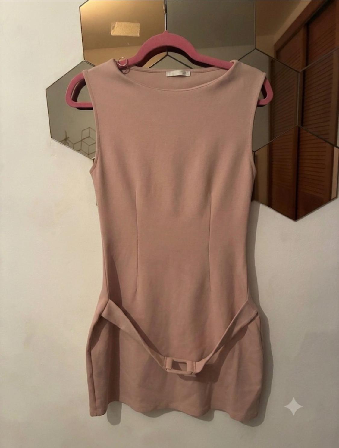 Short pink sleeveless dress with a matching belt, hanging on a pink hanger against a white wall with hexagonal mirrors.