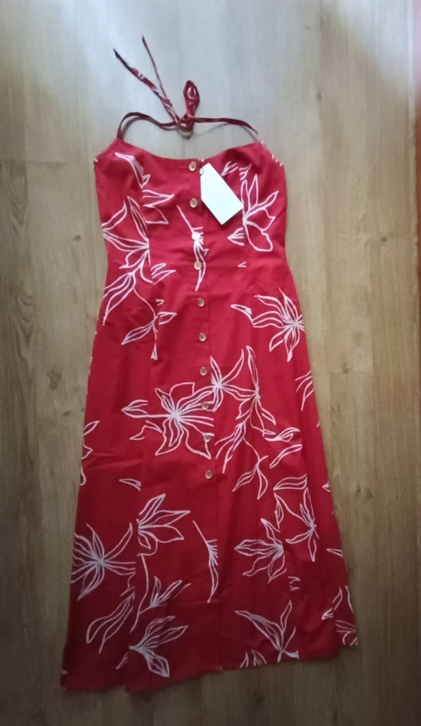 Red dress with a white floral print, halter neck straps and front buttons, laid out on a wooden floor.