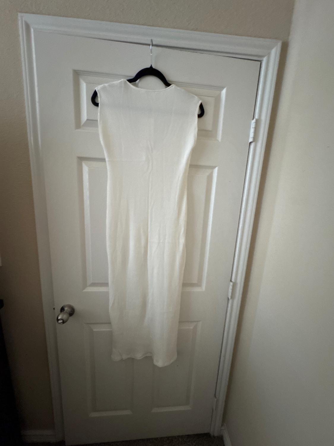 Sleeveless white dress hanging on a black hanger over a white door, in a well-lit indoor environment.