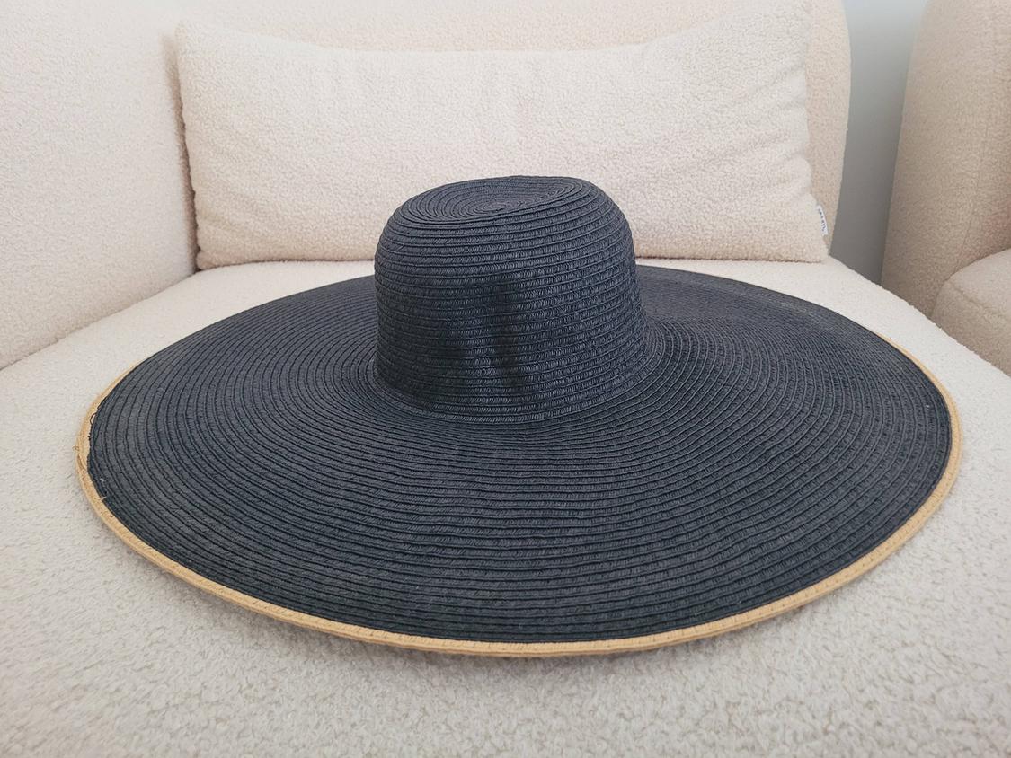 Black wide-brimmed hat on a beige sofa. The hat has a light brown trim and concentric line texture.