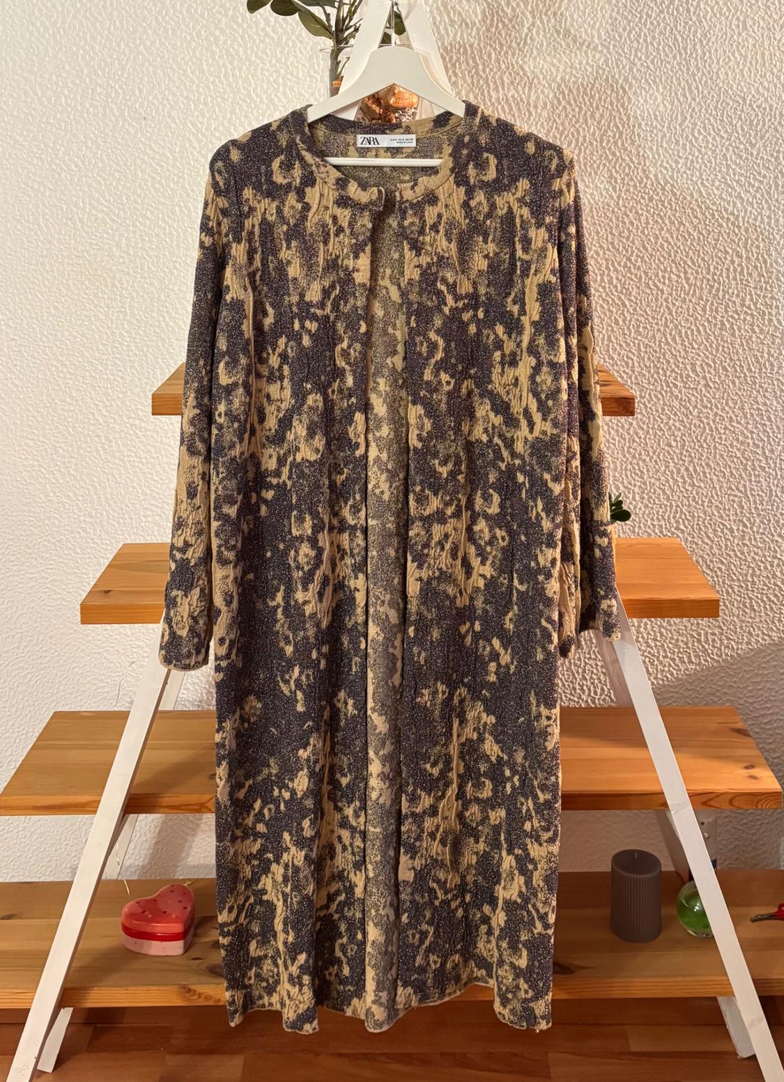 Patterned dress in brown and beige tones hanging on a white hanger over a wooden ladder. Visible tag: Zara.