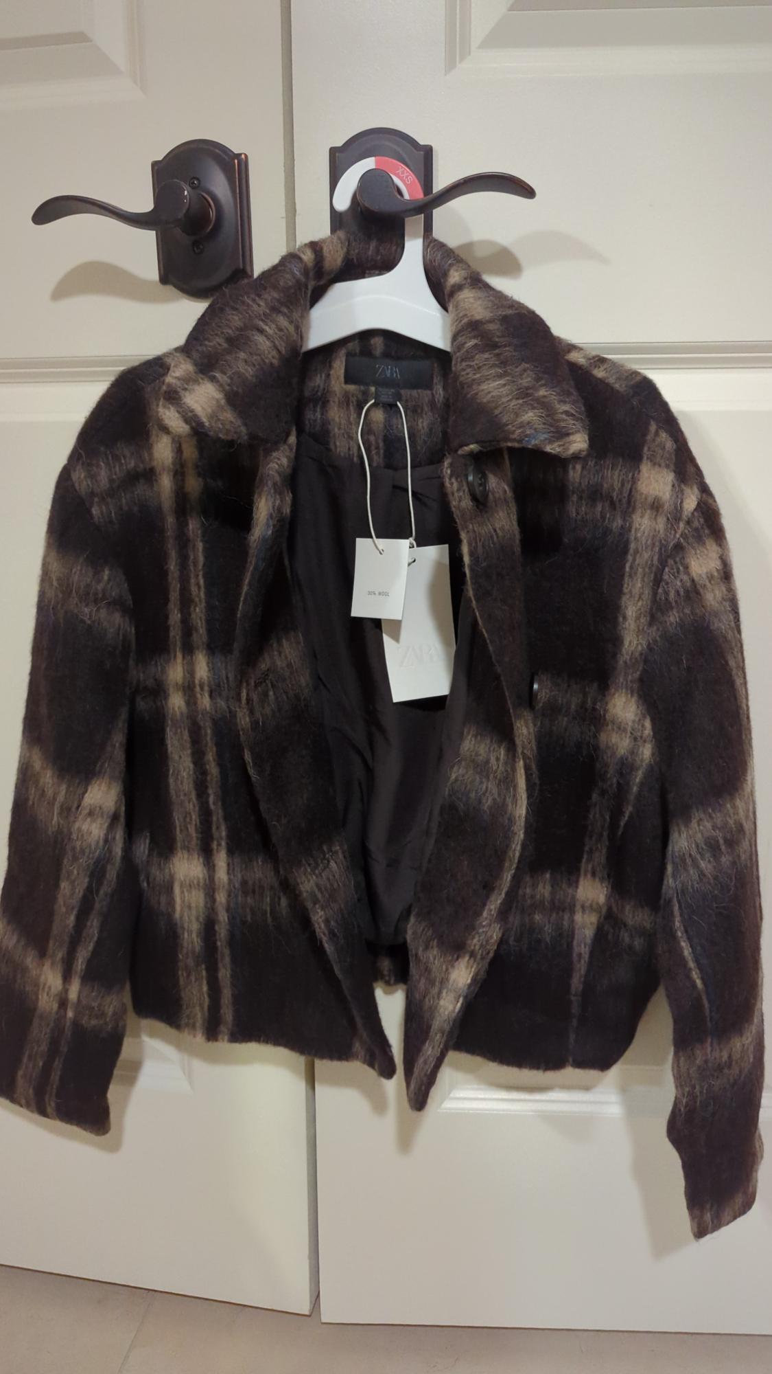 Brown and black checked jacket hanging on a white door. Visible label with text "20% wool" and "ZARA".