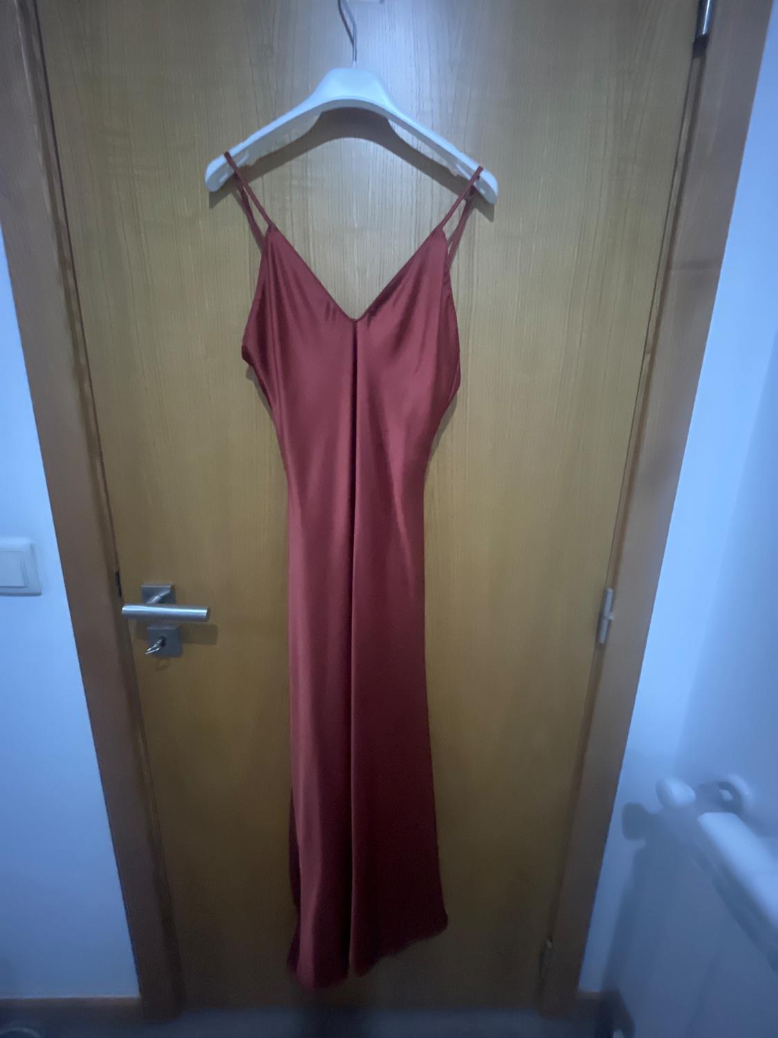 Copper-red satin maxi dress with thin straps and a V-neckline, hanging on a white hanger over a wooden door.