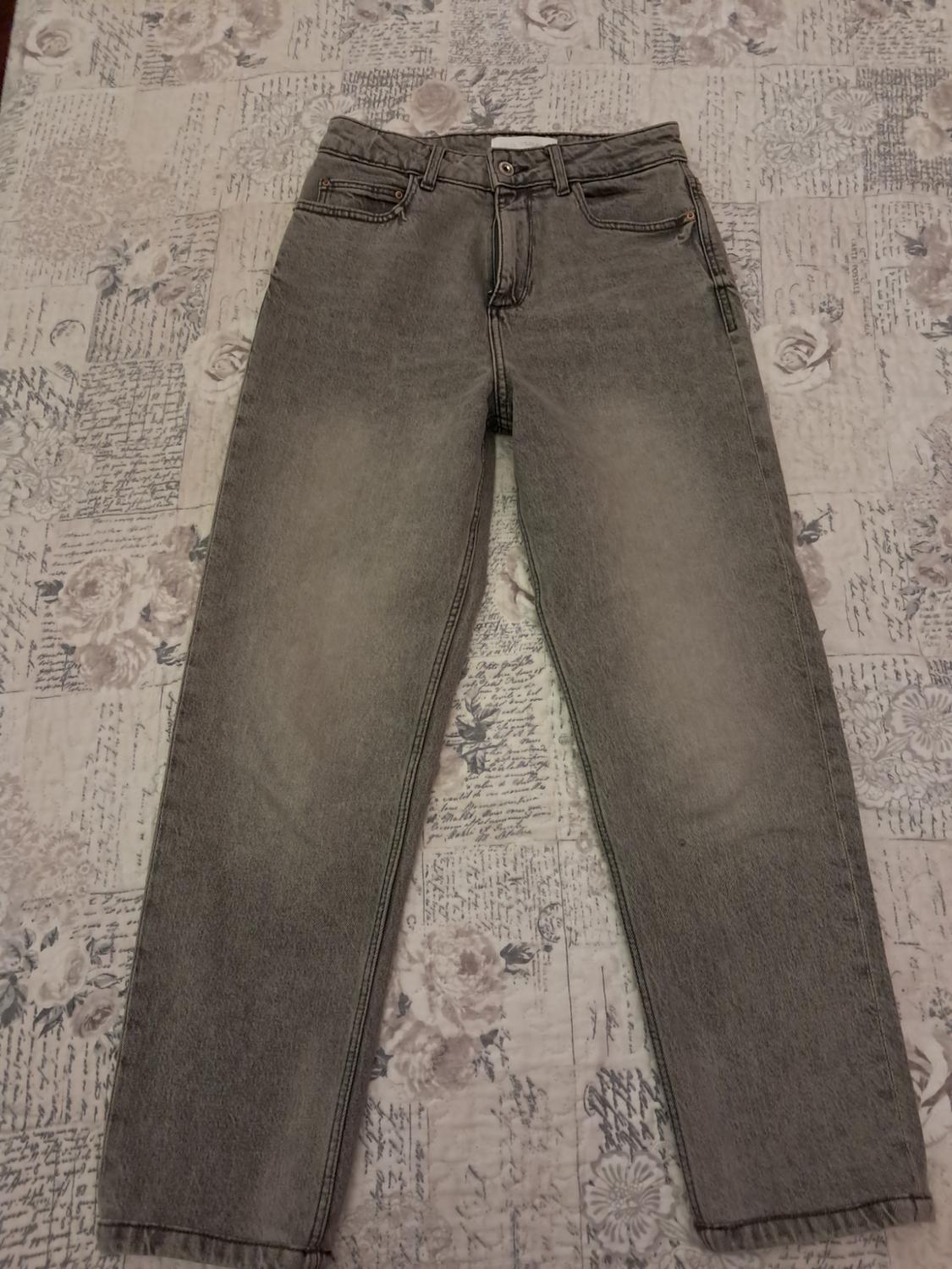 Grey denim trousers on a fabric background with a floral print and antique writing. Casual style.