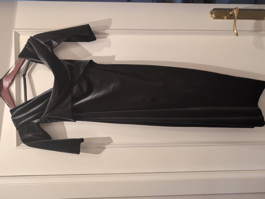 Long black velvet dress with a wrap neckline and sleeves, hanging on a hanger over a white door with a gold handle.