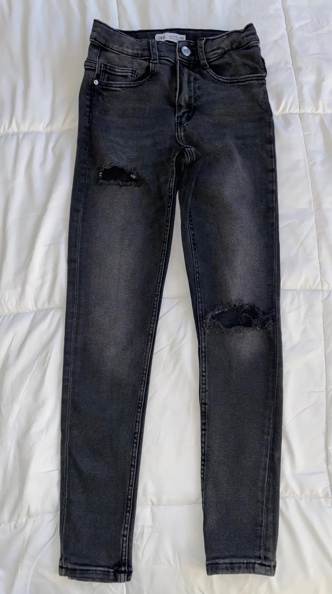 Front view of black pants with ripped knees and front pockets.
