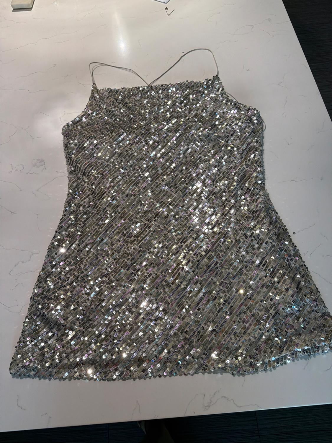 Short spaghetti-strap dress with silver sequins in diagonal lines, laid out on a white marble surface.