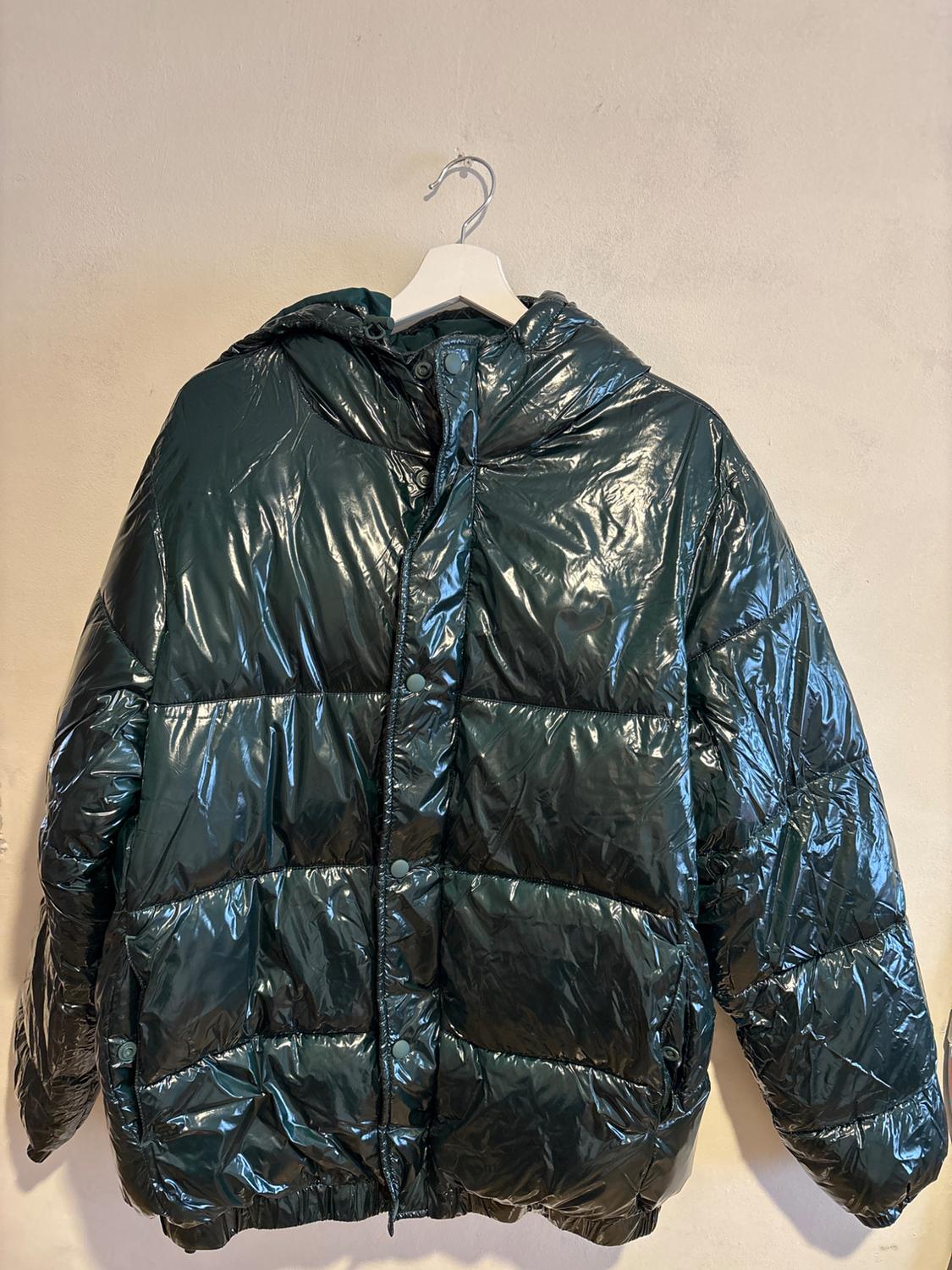 Dark green quilted jacket with a glossy finish, hanging on a white hanger against a beige wall.
