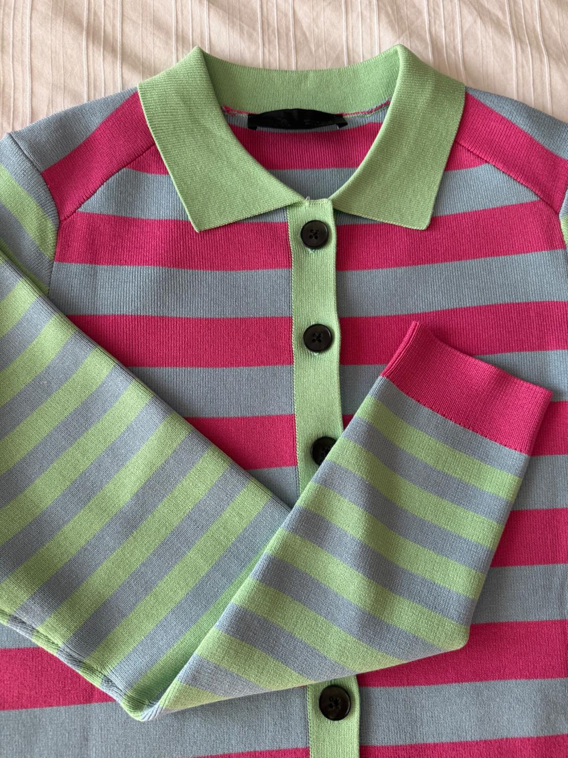 Horizontal striped shirt in pink, green, and grey with black buttons. Green collar and beige fabric background.