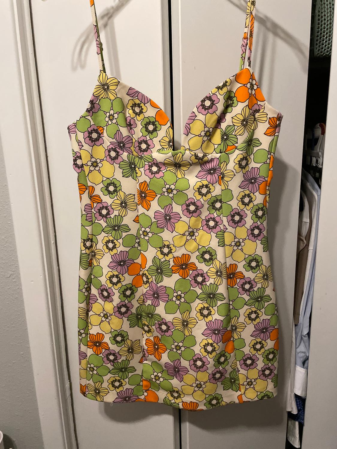 Vestido camisero con estampado floral en tonos naranja, verde y morado, colgado de una puerta blanca.