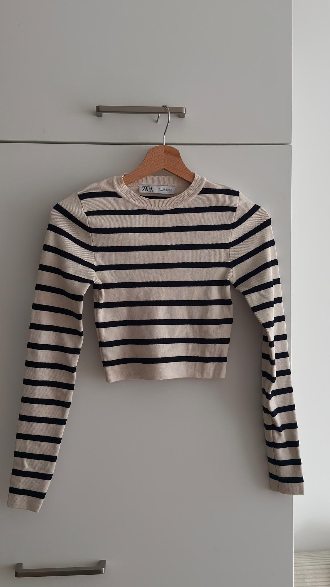 Black and beige striped jumper hanging on a wooden hanger in front of a white wardrobe. Visible tag: Zara.