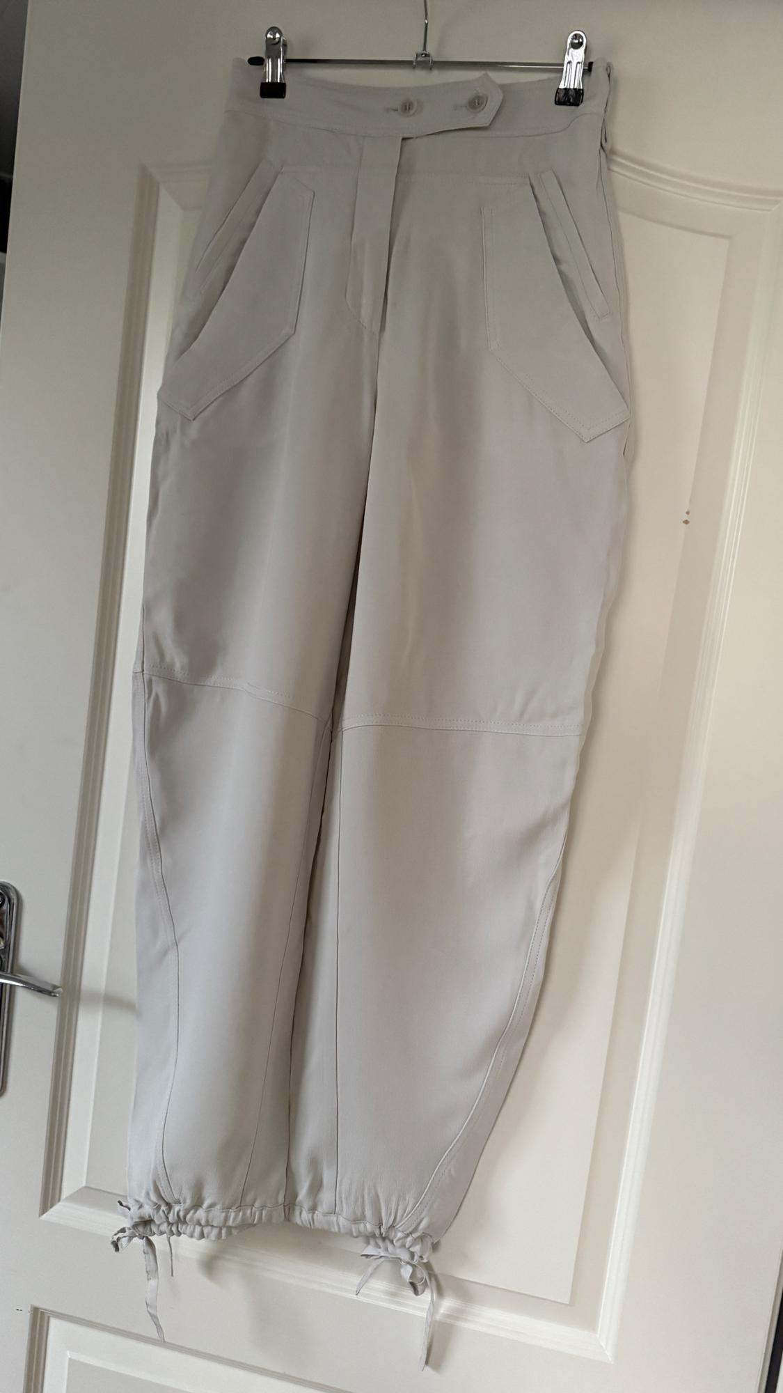 Beige trousers hanging on a white door, with large pockets and adjustable drawstrings at the ankles.