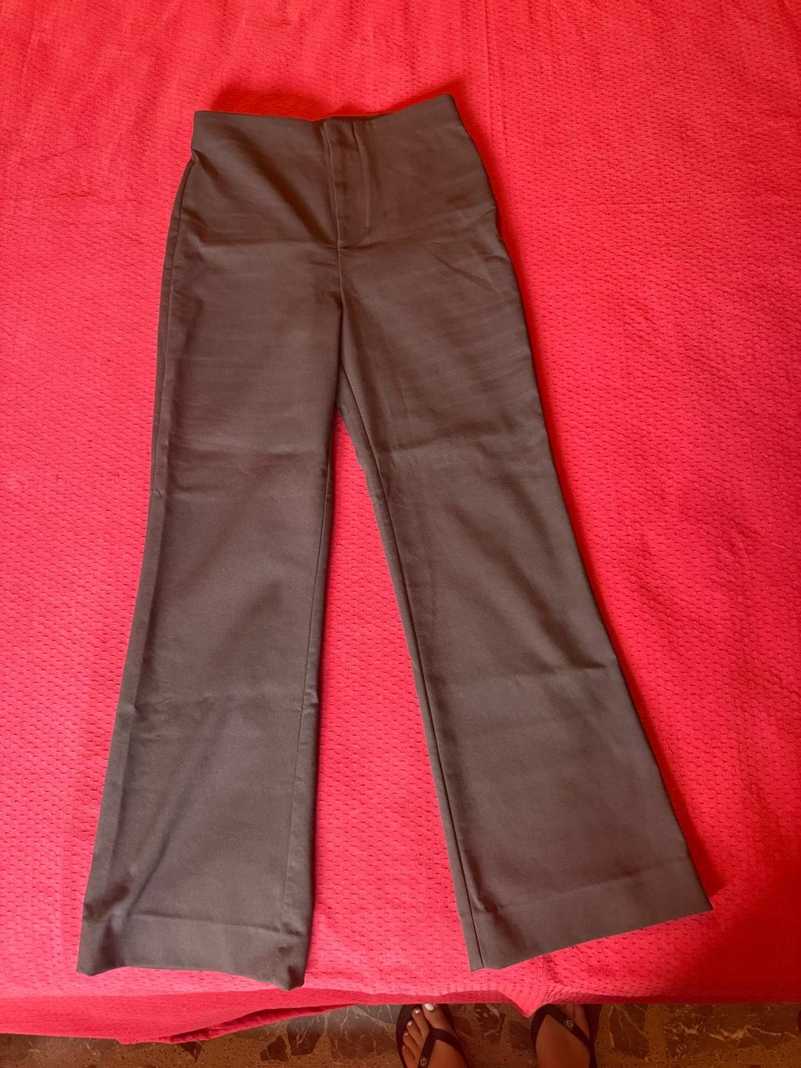 Dark high-waisted, straight-leg trousers, laid out on a red fabric surface. A pair of feet is visible at the bottom edge.