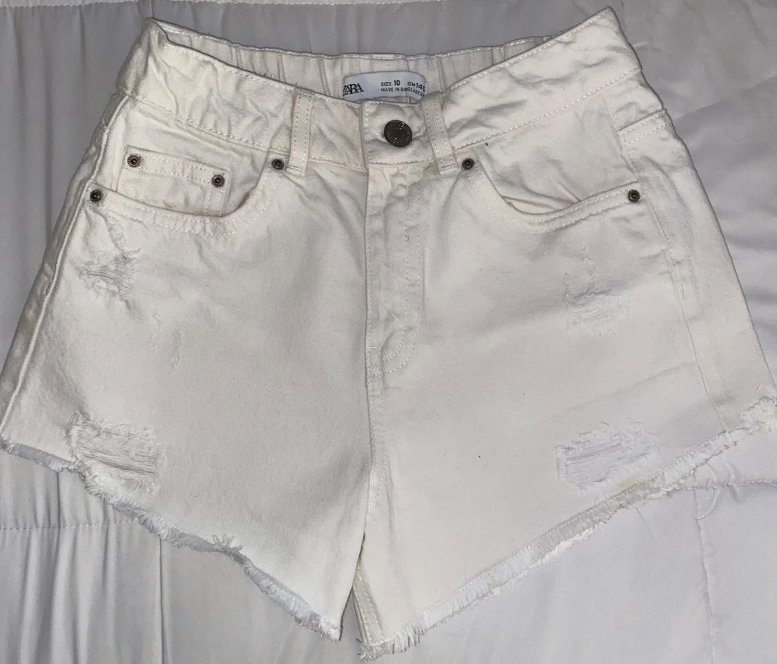 Front view of distressed white shorts with front pockets and a button.