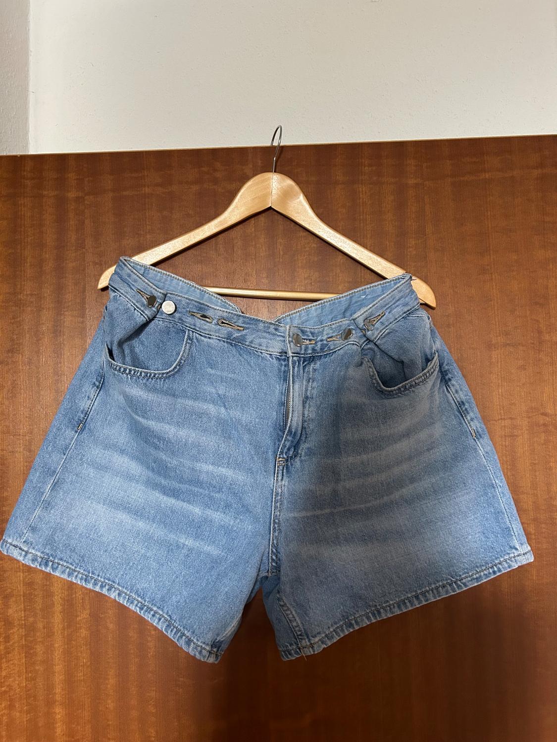 Light blue denim shorts with buttons at the waist, hanging on a wooden hanger in front of a door.