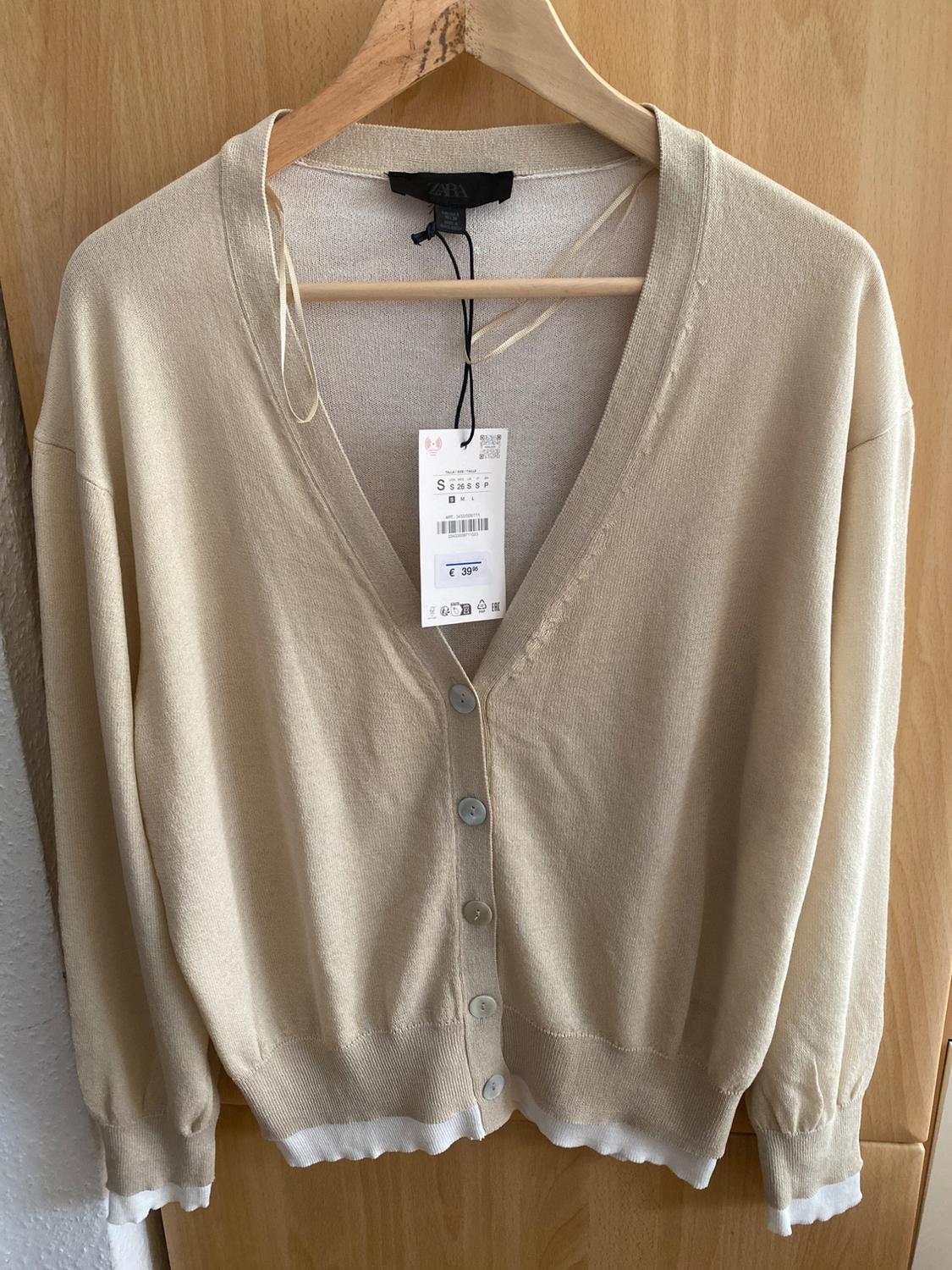 Beige cardigan hanging on a wooden hanger, with white buttons and a visible €39 price tag on the front.