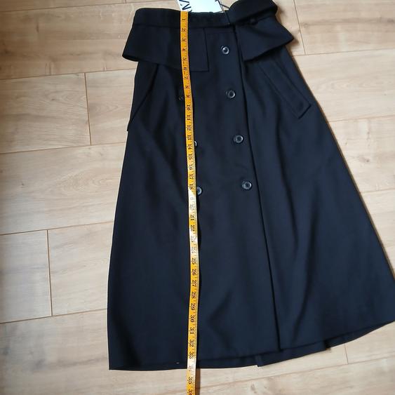Black skirt with buttons and a wide belt on a wooden floor. Yellow tape measure measures the skirt's length.