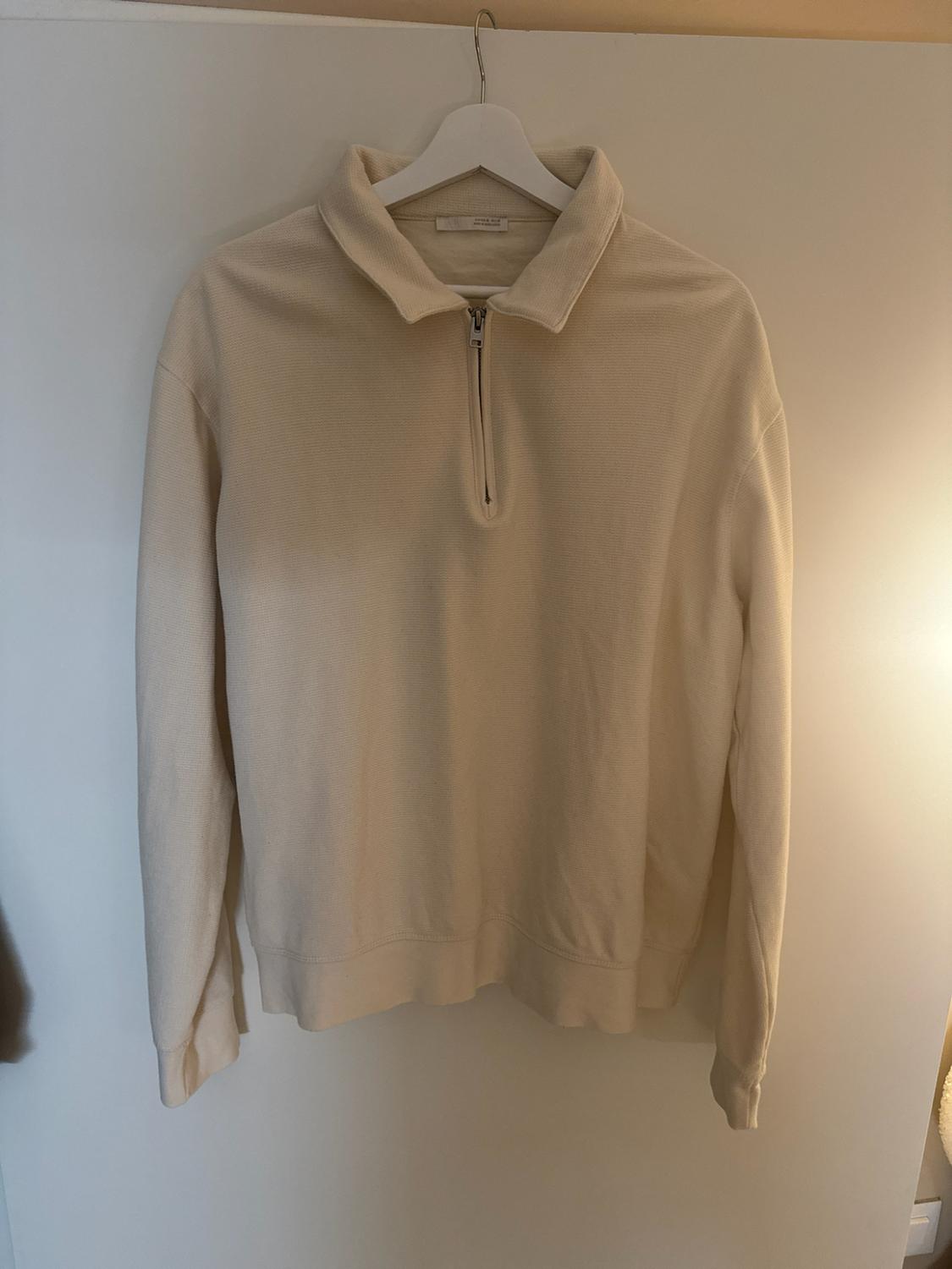 Cream long-sleeve polo neck jumper with a half zip, hanging on a white hanger on a door.