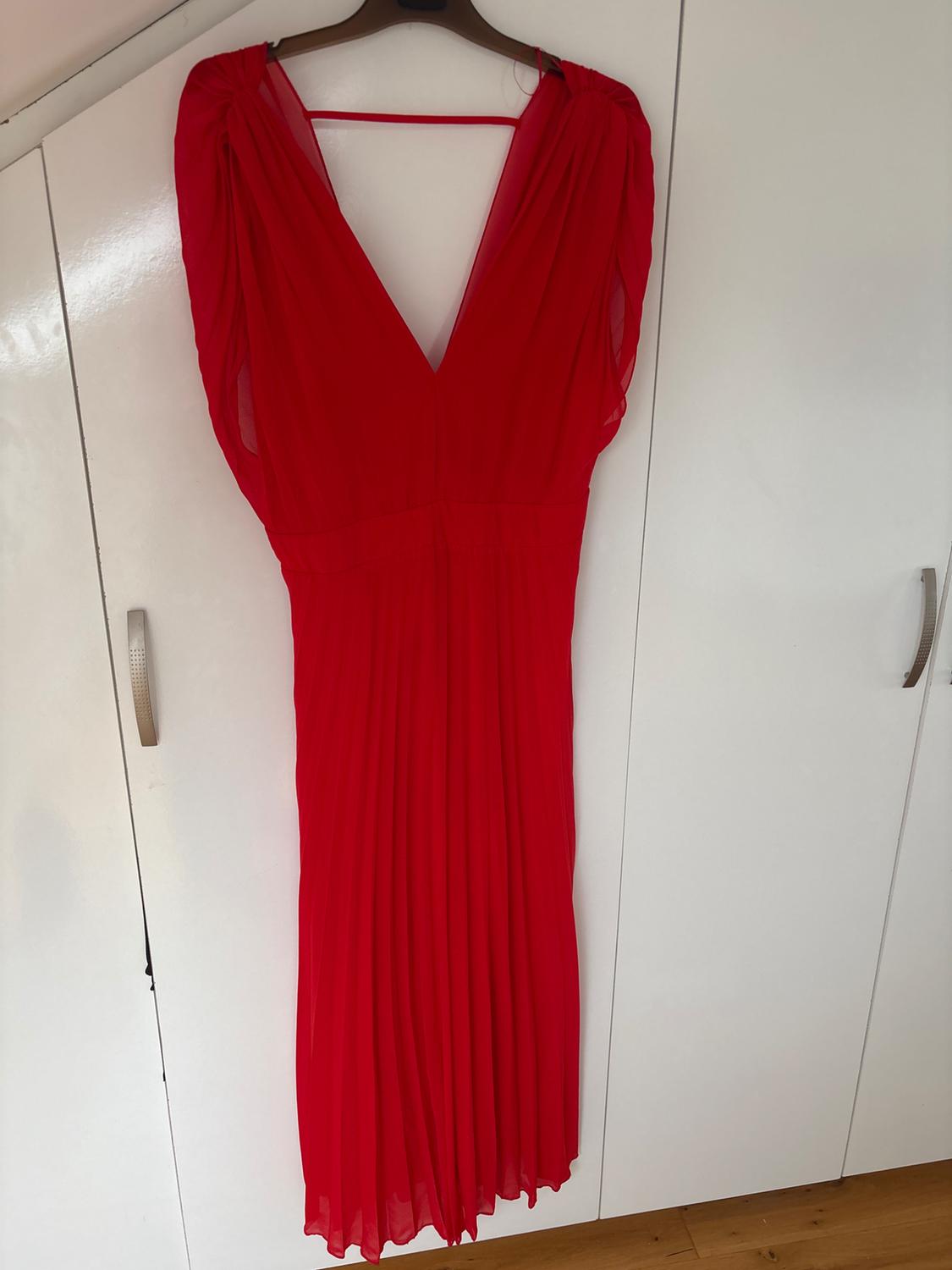 Red pleated V-neck dress hanging on a hanger in front of a white wardrobe.