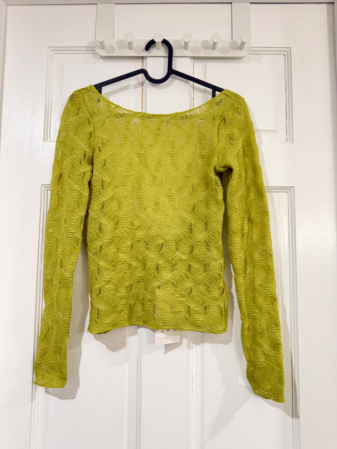 Textured green long-sleeved jersey hanging on a black hanger over a white door. Label visible at the bottom.