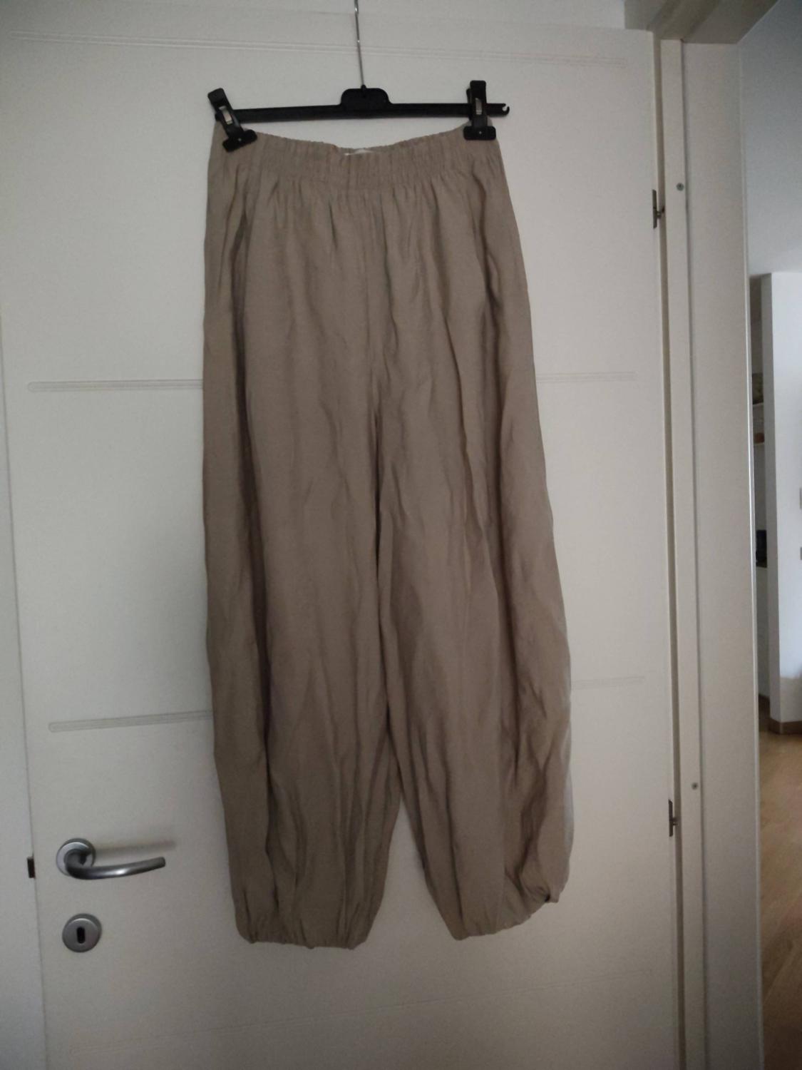 Beige φard[sic - loose/baggy]... Wait, let's use proper Greek localization:
Μπεζ φαρd... -> Μπεζ φαρδύ παντελόνι με λάστιχο στη μέση και στους αστραγάλους, κρεμασμένο σε μια κρεμάστρα σε λευκή πόρτα.