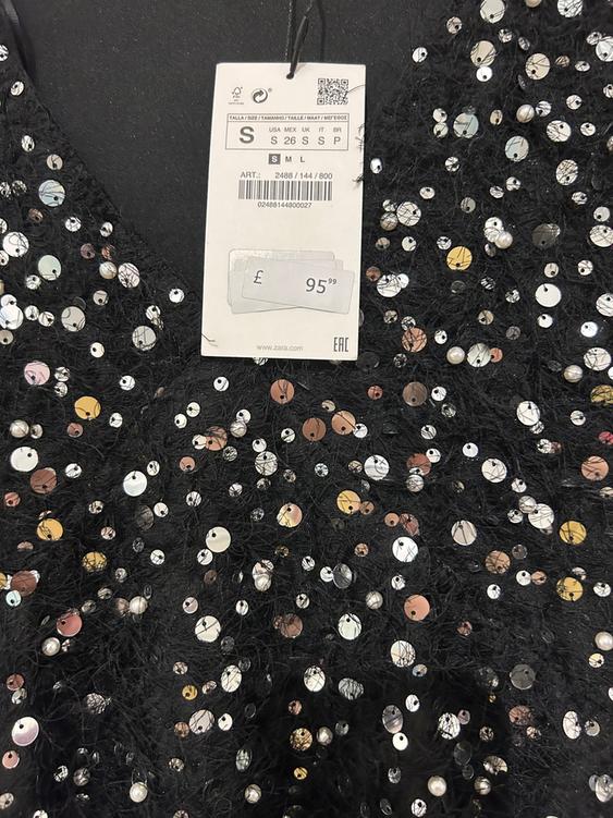 Price tag in pounds on black fabric with shiny sequins. Visible text: "£95.99", "S", "www.zara.com".