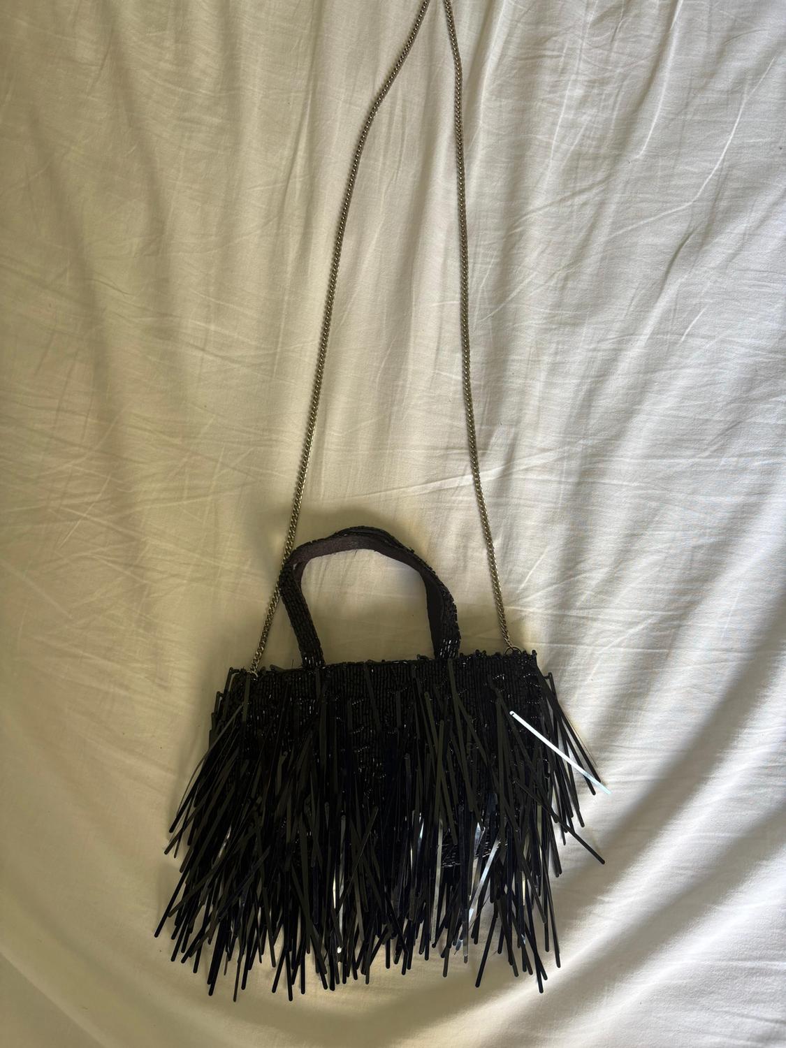 Black handbag with long tassels and a gold chain on crumpled white fabric.