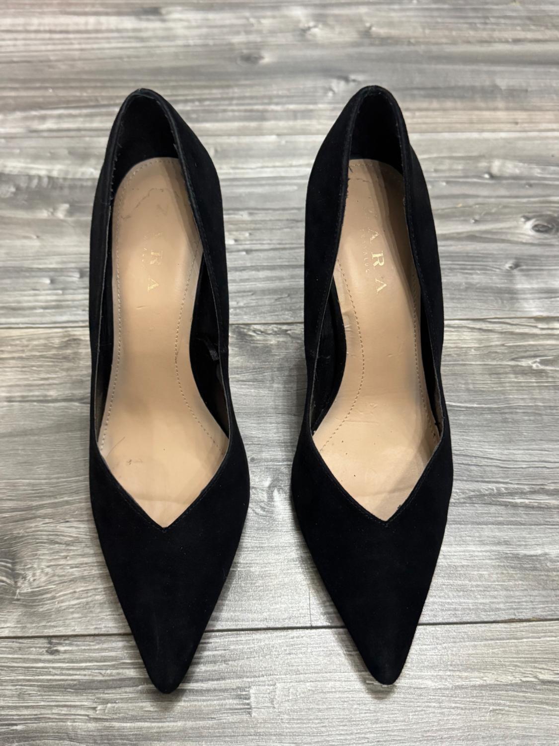 Black pointed-toe high-heeled shoes on a grey wooden floor. ZARA is written on the insole.