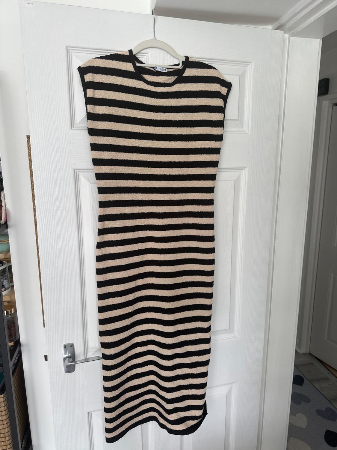 Black and beige horizontal striped dress hanging on a white coat hanger over a white door in a well-lit interior.