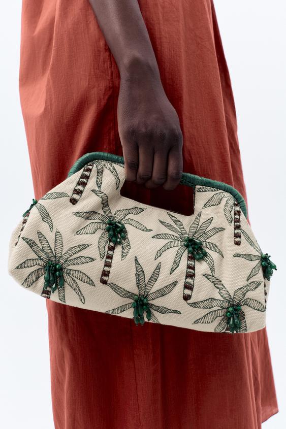 Detail surové kabelky s výšivkou zelených palem a korálky, integrovanou pevnou rukojetí a zeleným horním okrajem.