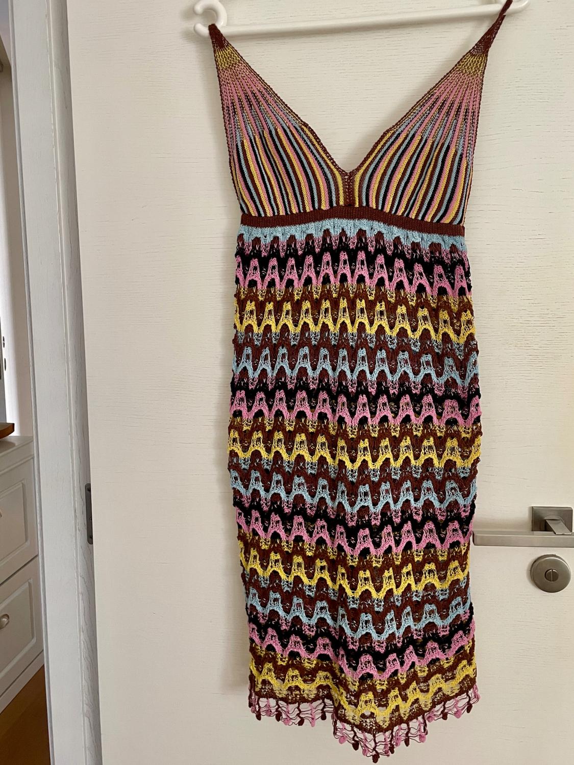 Multicoloured knitted dress hanging on a white door. It has a V-neck, a vertical striped bodice and a skirt with a zigzag pattern.