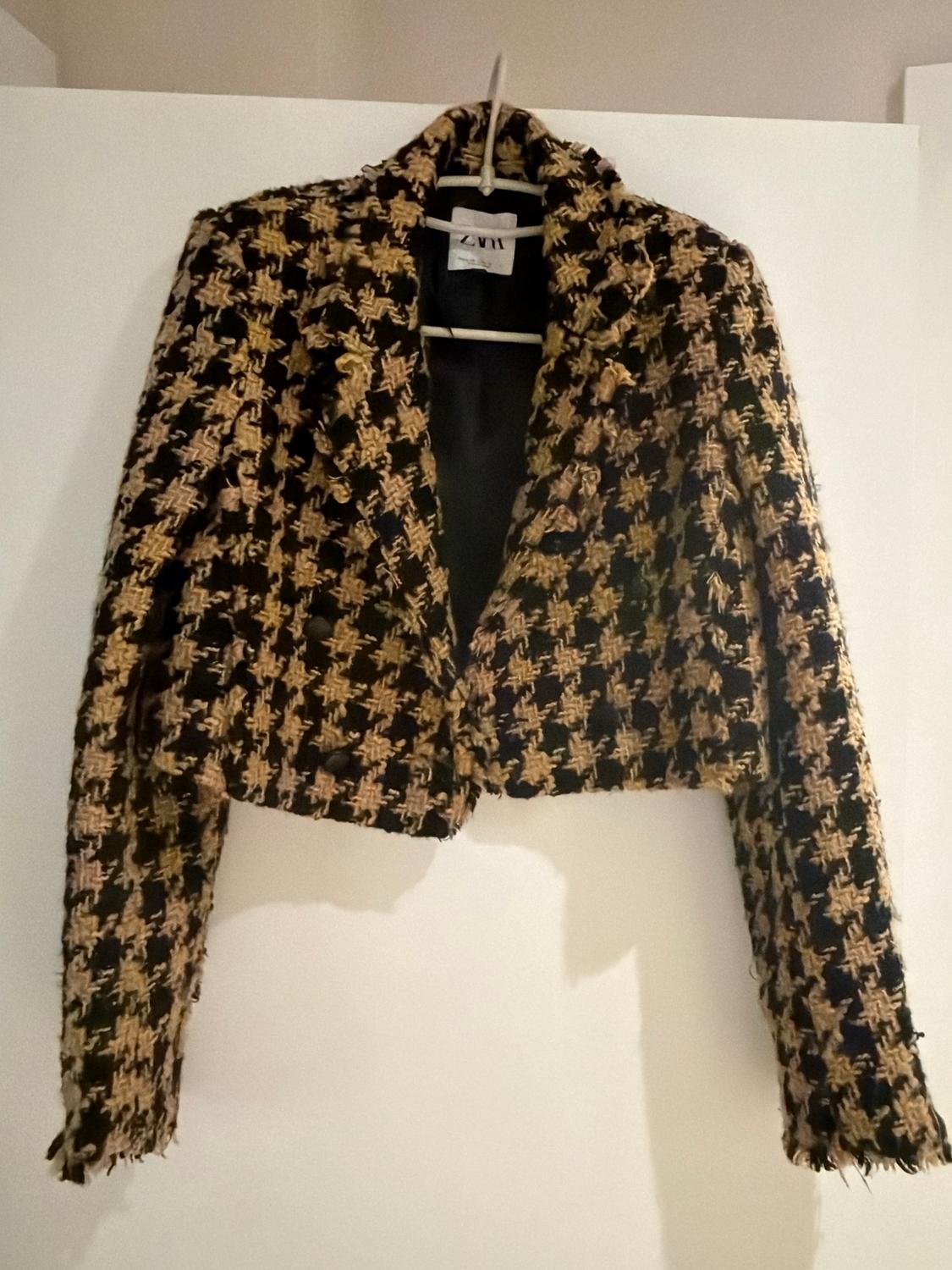 Short brown and black checked jacket hanging on a white hanger. Visible label with the text "ZWM".