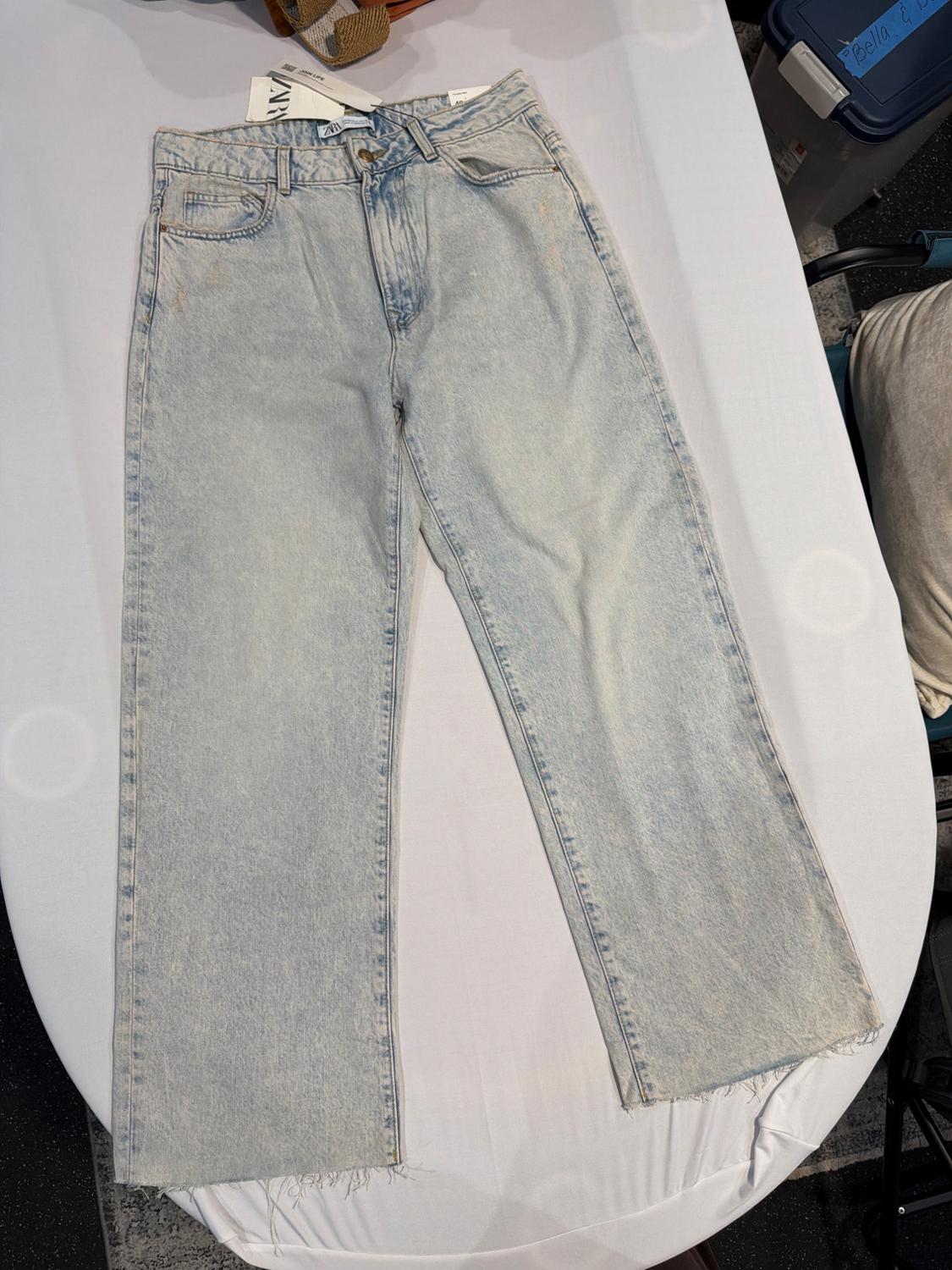 Light blue wide-leg jeans with frayed hems on white fabric. Text: ZARA, JOIN LIFE and Bella & in a blue box in the background.