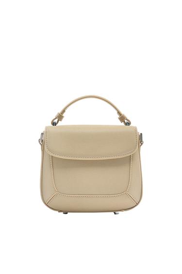 Small beige handbag with a top handle, front flap, and geometric stitching details on a white background.
