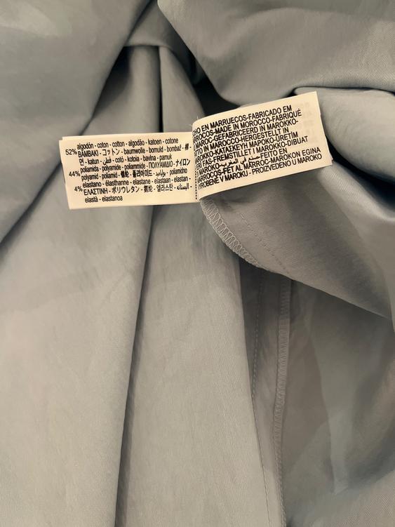 Multi-language fabric composition label on grey fabric. States 52% cotton, 44% polyamide, 4% elastane. Made in Morocco.