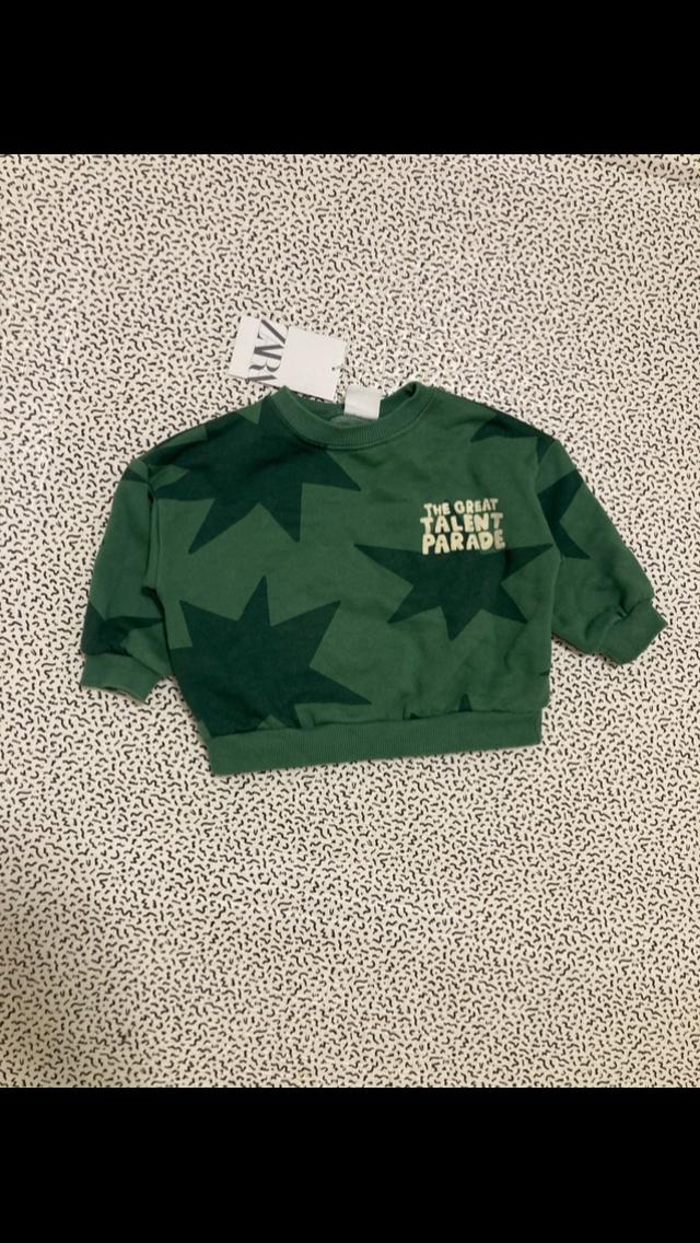 Green sweatshirt with dark stars and "THE GREAT TALENT PARADE" text on a white background with a black pattern. Visible label.