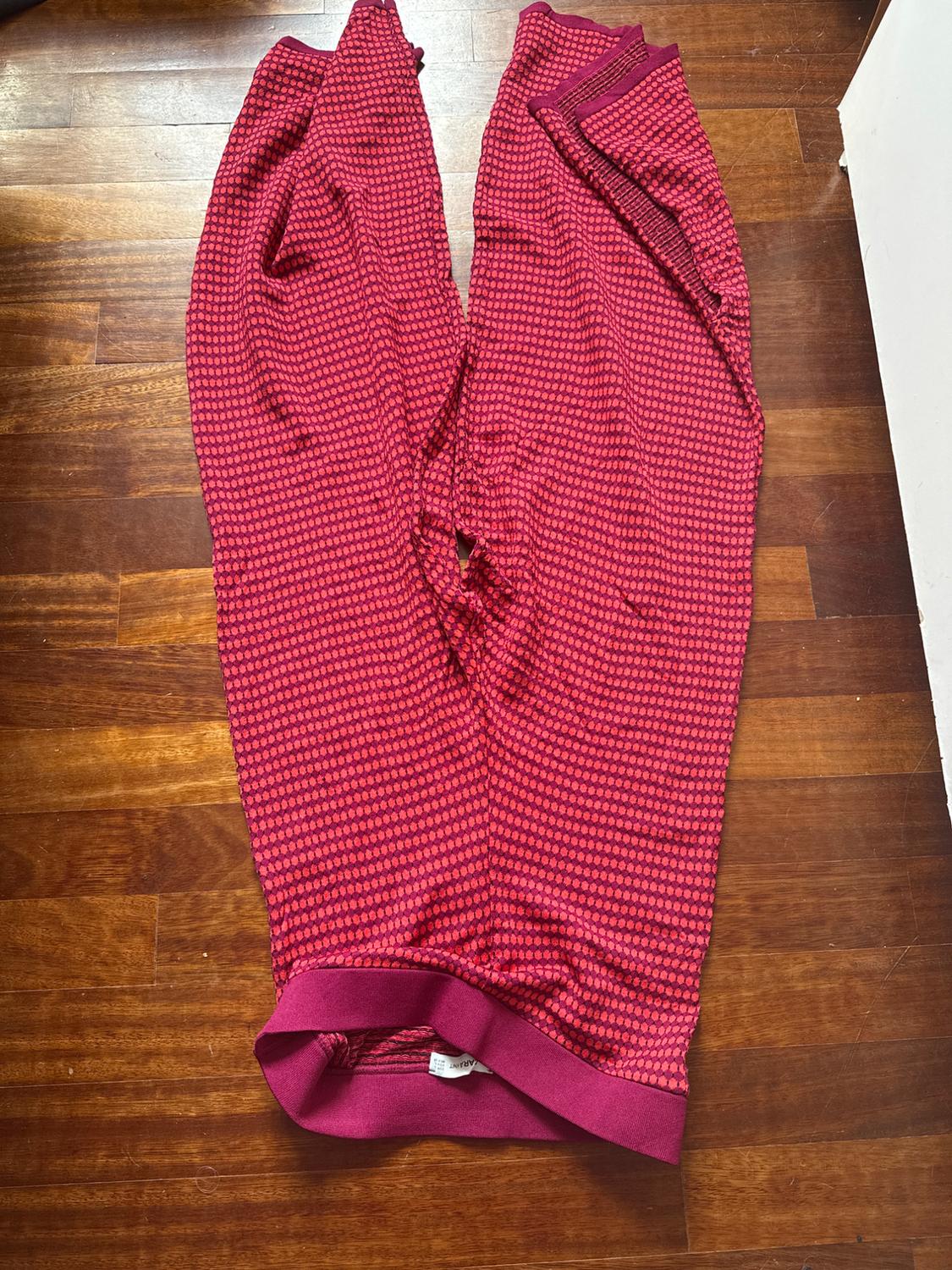 Red trousers with a small polka dot pattern on a wooden floor. The label is visible on the waistband.