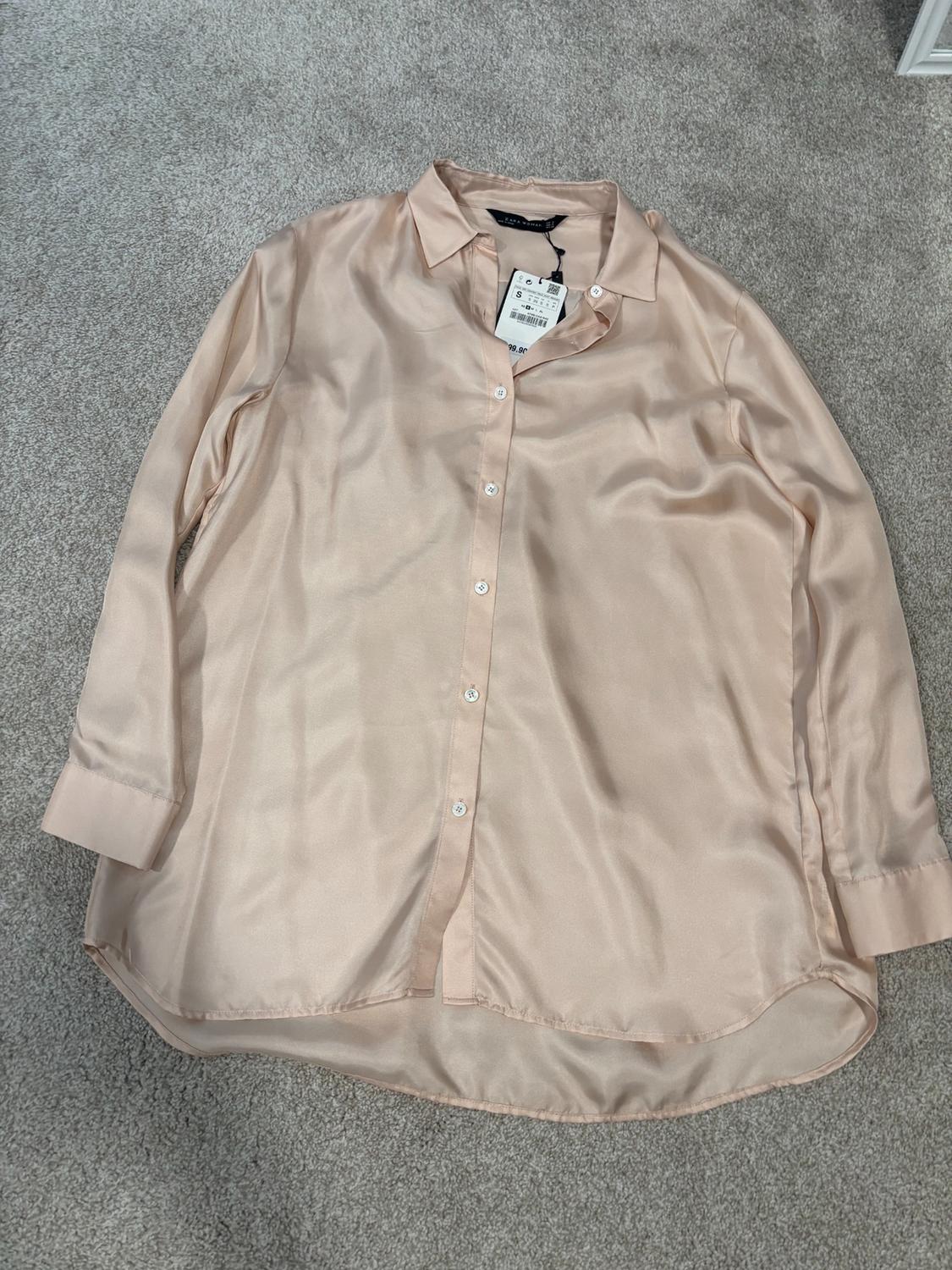 Light beige satin shirt with front buttons, placed on a gray carpet. Visible label on the collar.
