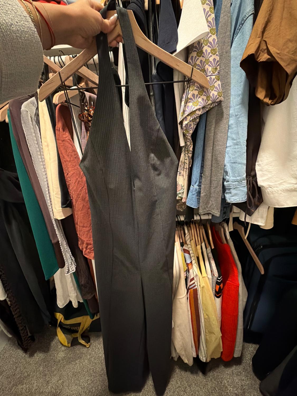 Hand holding a black jumpsuit in a closet full of clothes of various colors and styles, hanging on wooden hangers.