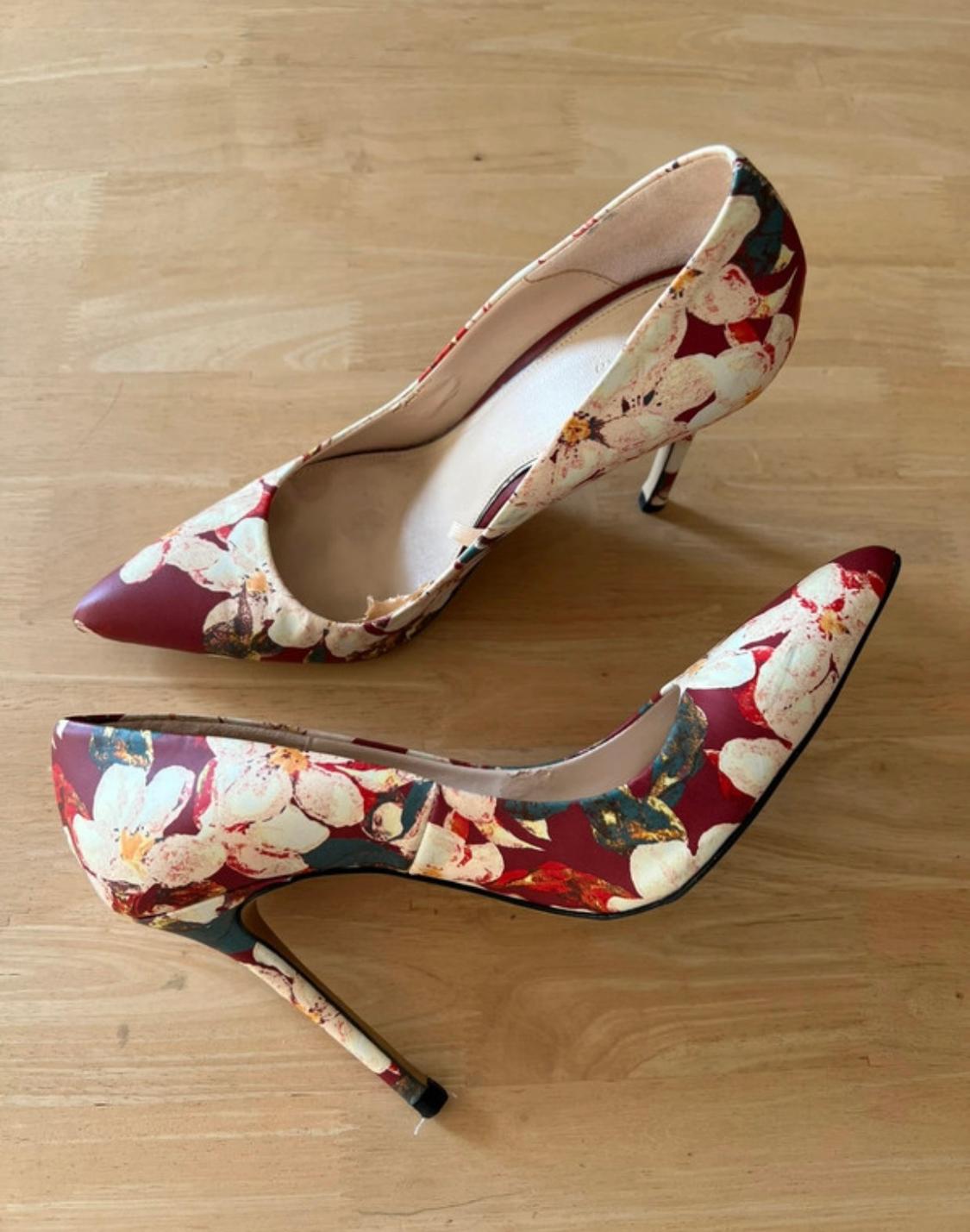 High-heeled shoes with a floral print in red and white tones on a light wooden surface.