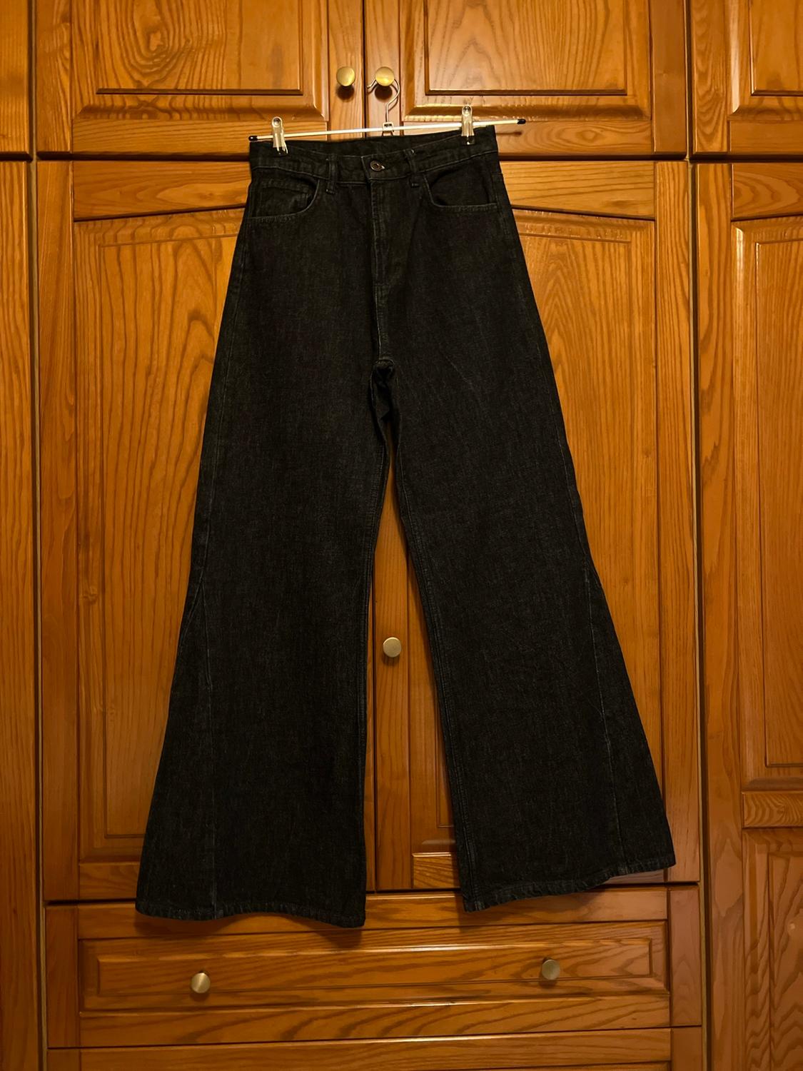 Black wide-leg jeans hanging on a hanger in front of a wooden wardrobe.