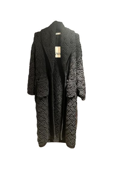 Long black knitted coat with intricate texture and large pockets. Visible label with the text "ZARA". White background.