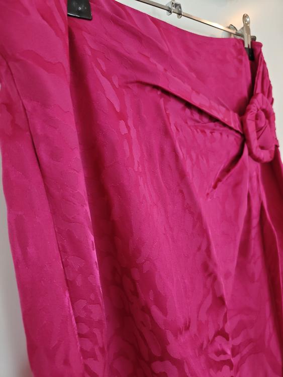 Fuchsia skirt with floral texture and bow detail at the waist, hanging on a metal hanger against a white background.