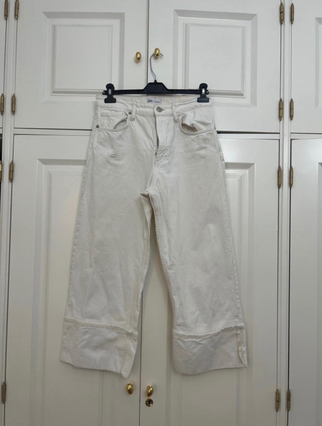 White wide-leg turn-up jeans, hanging on a black hanger in a white wardrobe with gold knobs. ZARA.