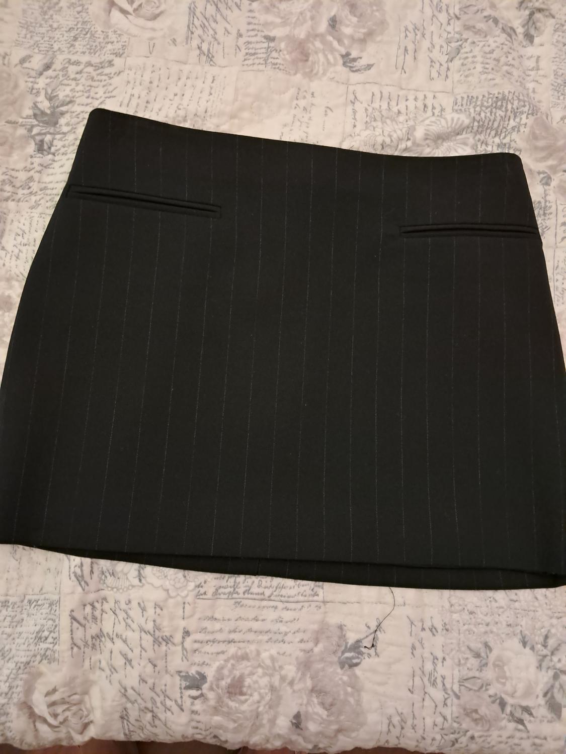 Black pinstripe mini-skirt with front pockets, against a fabric background featuring a floral print and handwritten text.