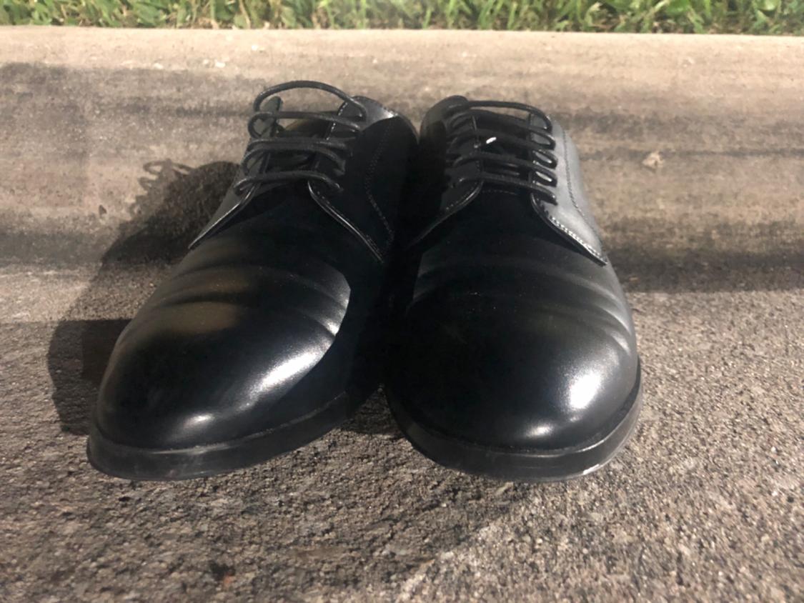 Black lace-up shoes resting on an asphalt curb. Night lighting that highlights the shine of the footwear and creates shadows.
