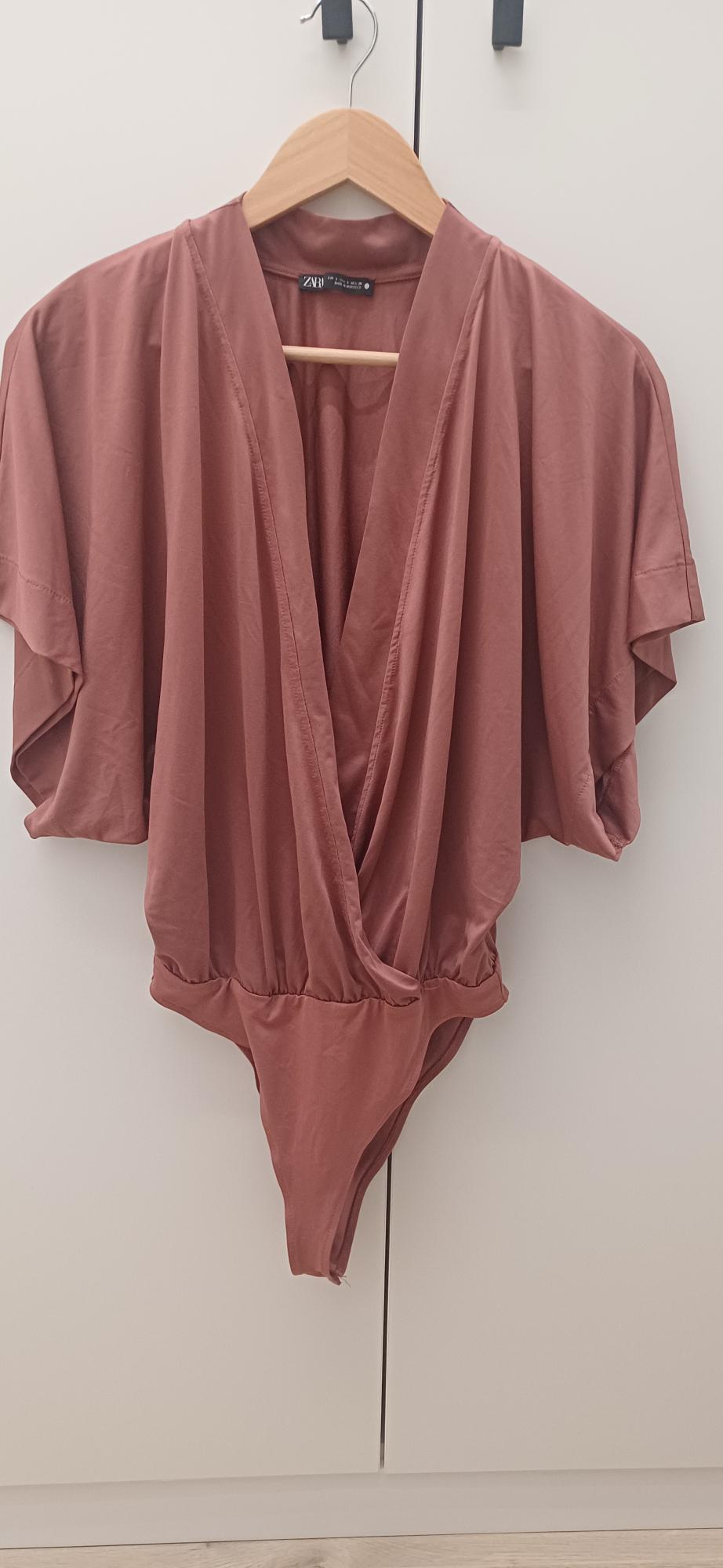 Pink draped bodysuit with a crossover neckline and short sleeves, hanging on a wooden hanger against a white background. Text on the label: ZARA.