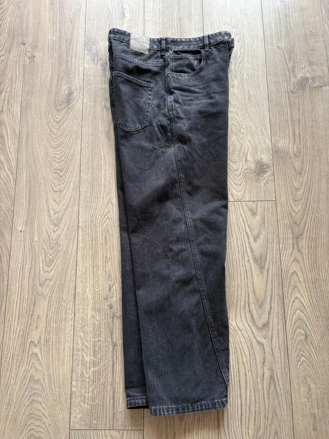 Black jeans folded on a wooden floor. Top-down casual style view showing the back pocket and a patch.