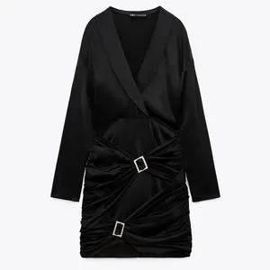 Black long-sleeved dress with a V-neckline and buckle details on the skirt. White background.