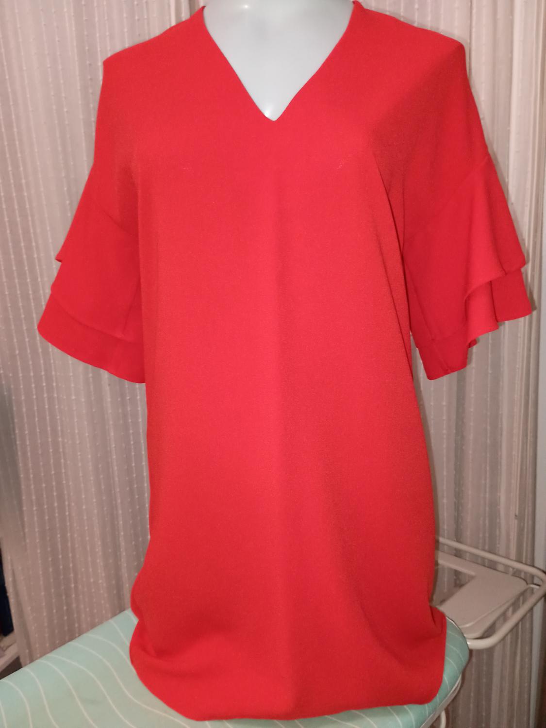 Red dress with short ruffled sleeves on a mannequin, against a background of light curtains.